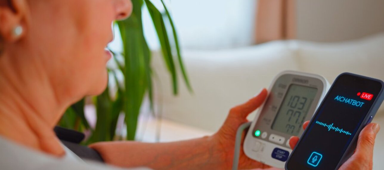 Ältere Frau mit Blutdruckmessgerät und Smartphone mit einer geöffneten Health-App.