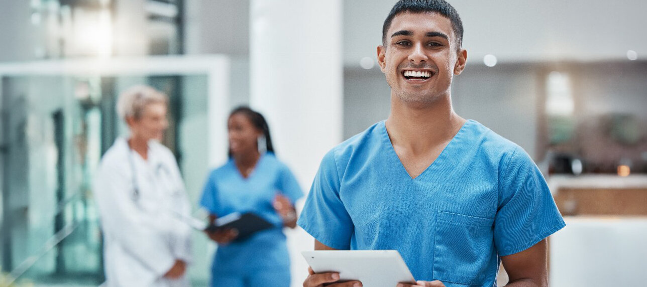 Junger männlicher Pfleger im Krankenhaus mit Tablet, lächelnd, der kamera zugewandt.