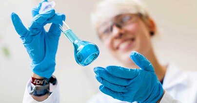 Kobieta w czepku i fartuchu laboratoryjnym potrząsa probówką