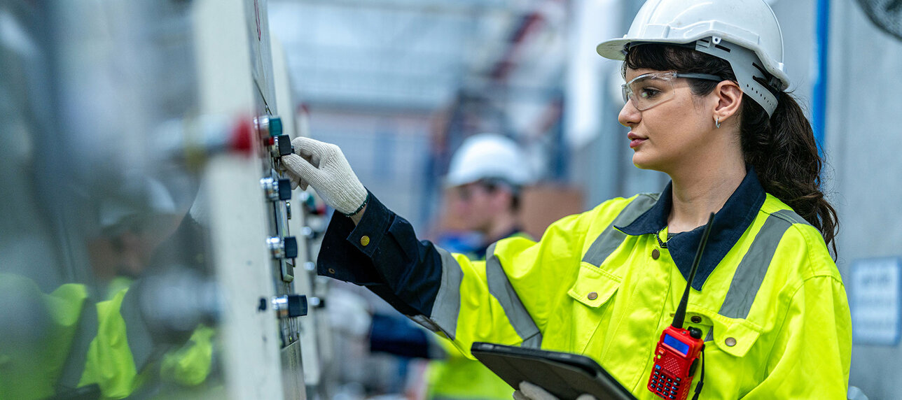 Männliche und weibliche Ingenieure in gepflegter Arbeitskleidung bereiten das Produktionssystem großer moderner Maschinen in einer Fabrik für industrielle Technologieprodukte vor und kontrollieren es.