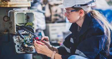 Elektrotechnikerin überprüft den Stromverteilungsschrank im Kontrollraum einer industriellen Produktionsstätte.