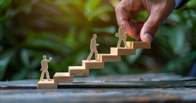 Businesspersonen aus Speerholz gehen eine freistehende Modelltreppe hoch. Symbol für ein Coaching-Konzept, für persönliches Wachstum und Entwicklung.